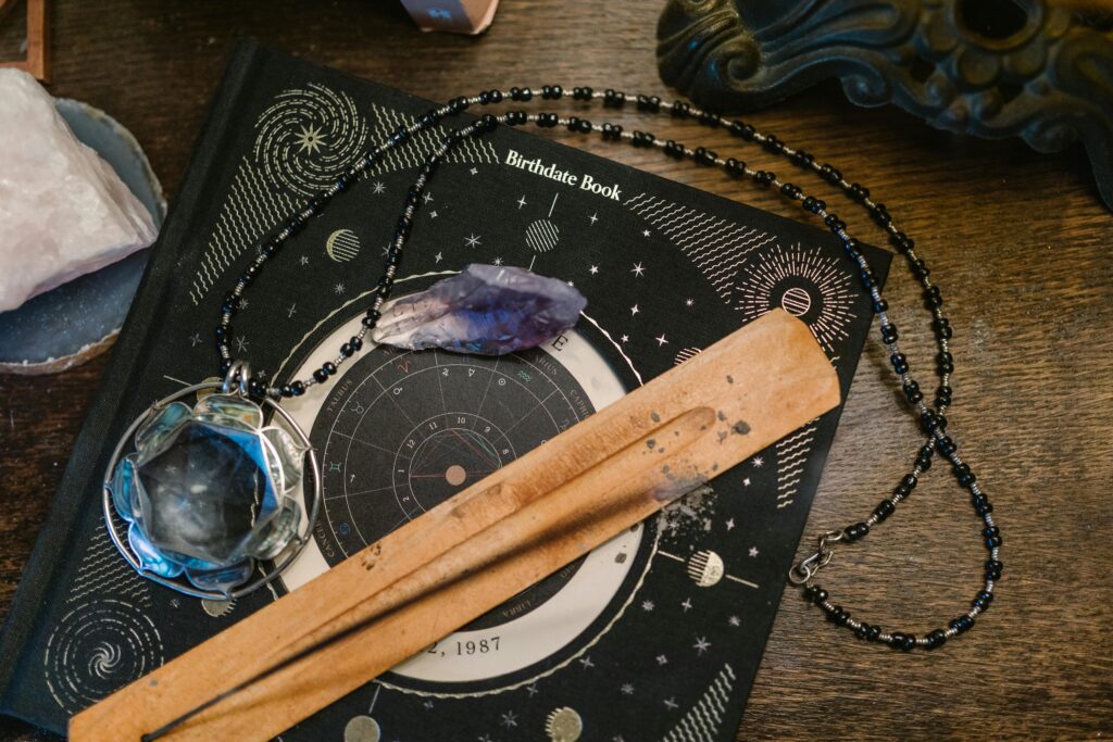 Healing crystals placed on an astrology birth chart book alongside a crystal pendant, amethyst point, and incense holder on a wooden table.