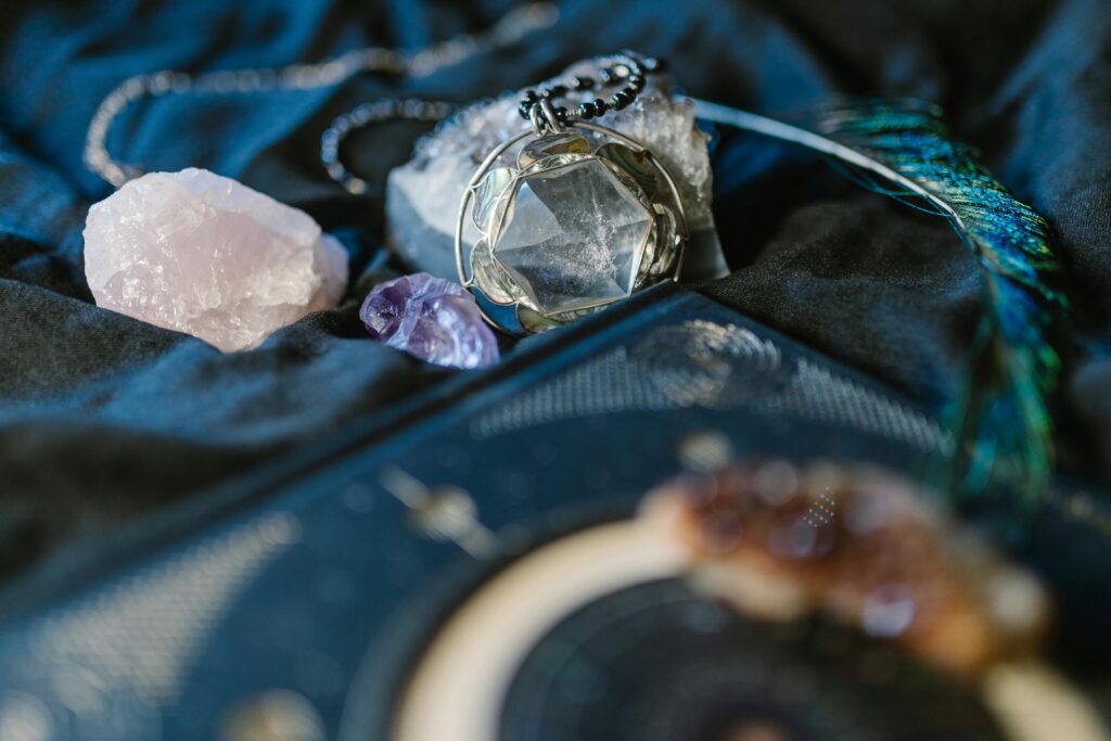 Healing crystals such as rose quartz, amethyst, and clear quartz displayed with spiritual jewelry and ritual tools on a dark cloth.