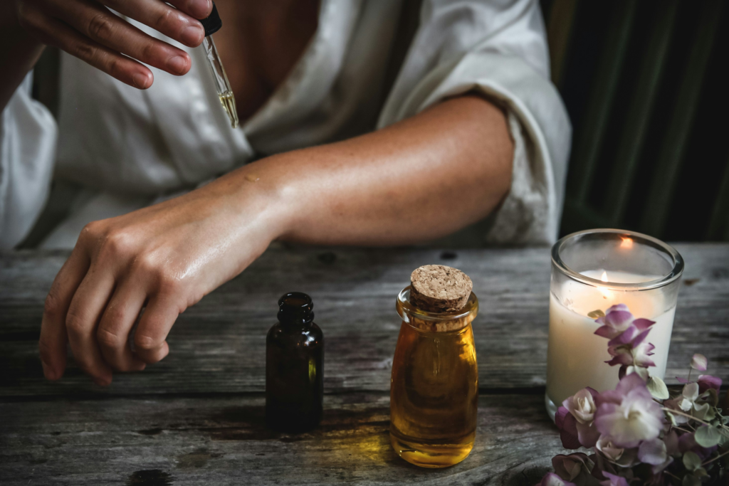 Person applying essential oil to the skin beside candles and glass bottles, illustrating essential oils benefits for relaxation, self-care, and mindful rituals.