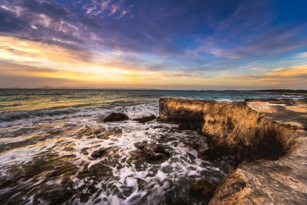 Rocky coastline at sunset where ocean waves meet ancient stone, symbolising the natural force of energetic points around the world.