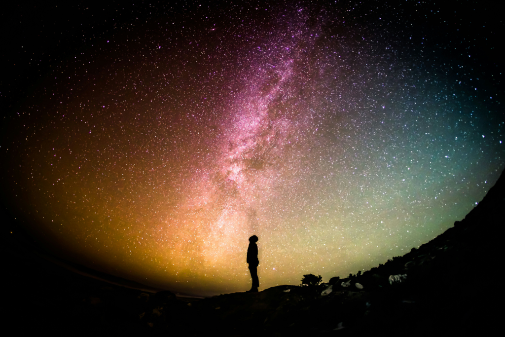 Silhouette of a person standing beneath a vibrant Milky Way galaxy, gazing at the night sky in a moment of reflection and awe