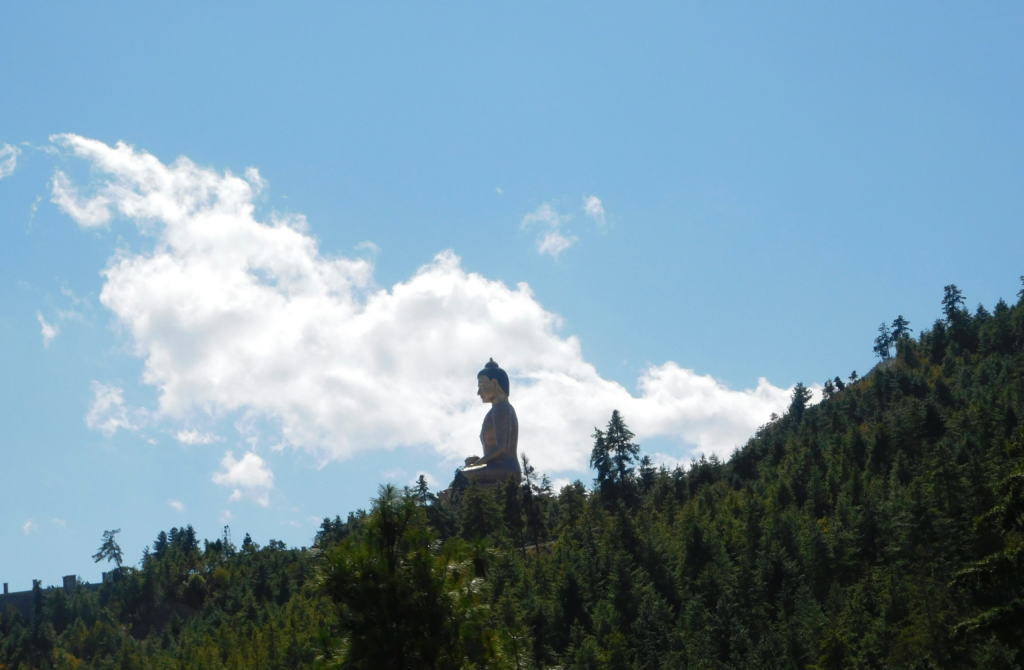 Large Buddha statue overlooking a forested hillside beneath a clear blue sky, symbolising stillness and spiritual contemplation