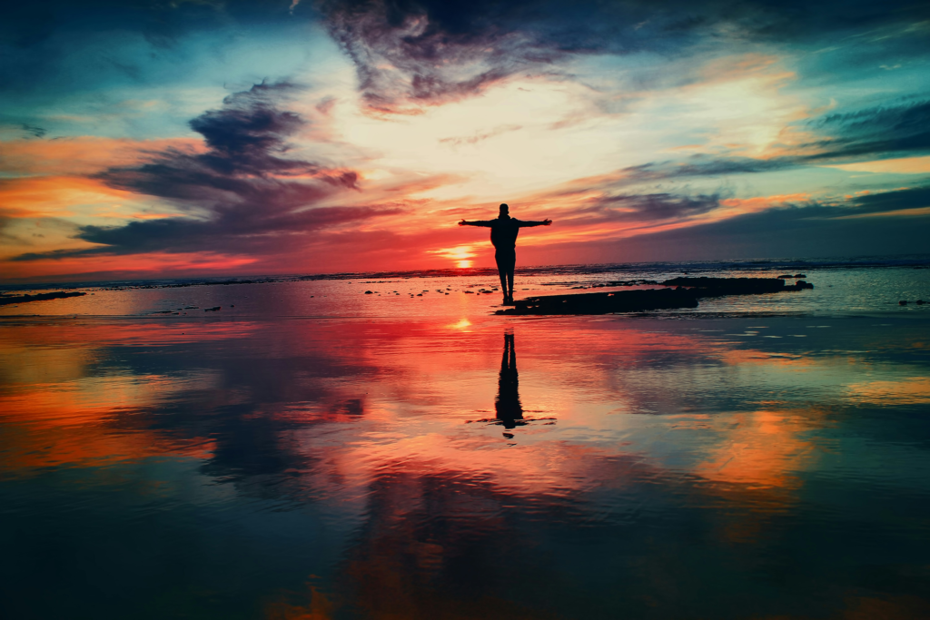 Silhouette of a person standing with arms open at sunset, reflecting inner peace, alignment, and a deep connection with nature