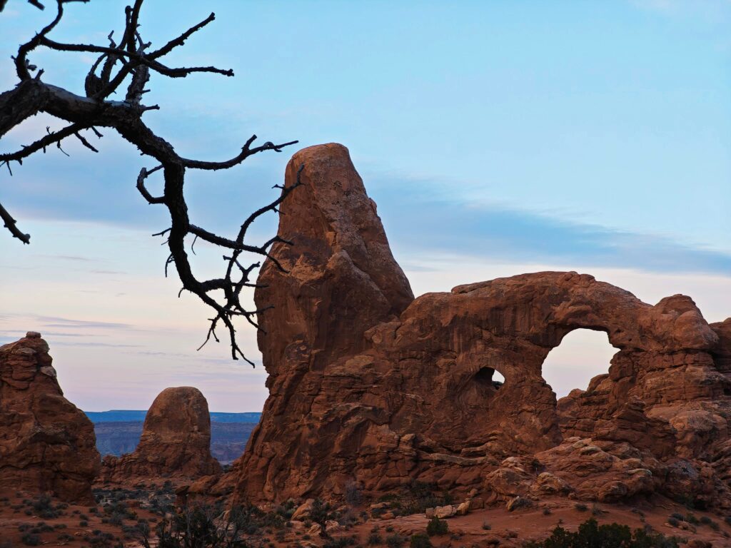 Natural rock arch formation in a desert landscape at dusk, with weathered stone structures and open sky.