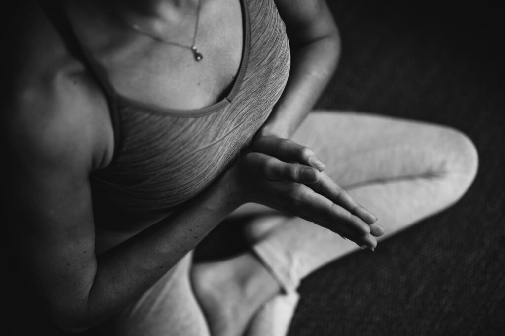 Person sitting in a calm meditation pose with hands together, focusing on breath and inner stillness