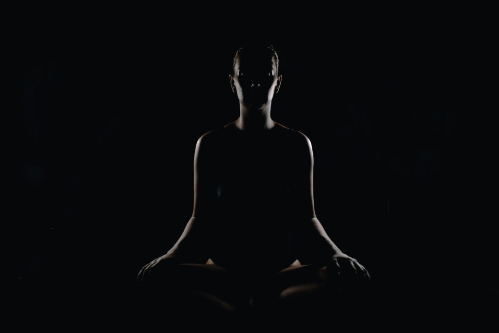 Silhouetted figure sitting in a meditative posture against a dark background, symbolising stillness, inner awareness, and deep self-reflection.