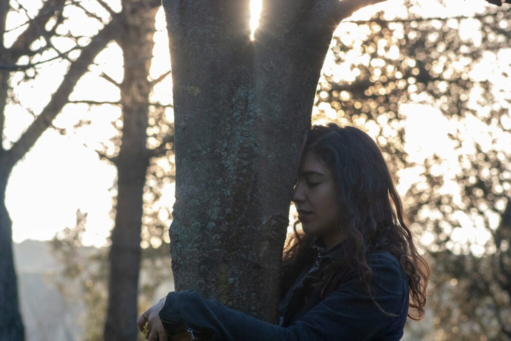 A person gently embracing a tree in a forest, symbolising connection with nature, grounding energy, and emotional balance.